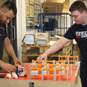 (v. l.) Adem Kaya und Moritz Kesting zu sehen, die den Besuchern den Aufbau eines Lagers mithilfe eines kleinformatigen Übungsmodells erklären.